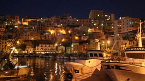 Une ville côtière nocturne, avec des bateaux amarrés dans le port et des bâtiments illuminés par des lumières chaleureuses.