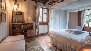 Un dormitorio con cama a dosel, muebles de madera, una araña y vistas al exterior.