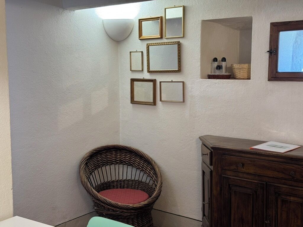 A room with a wicker chair, a wooden cabinet, and several framed mirrors on the wall.