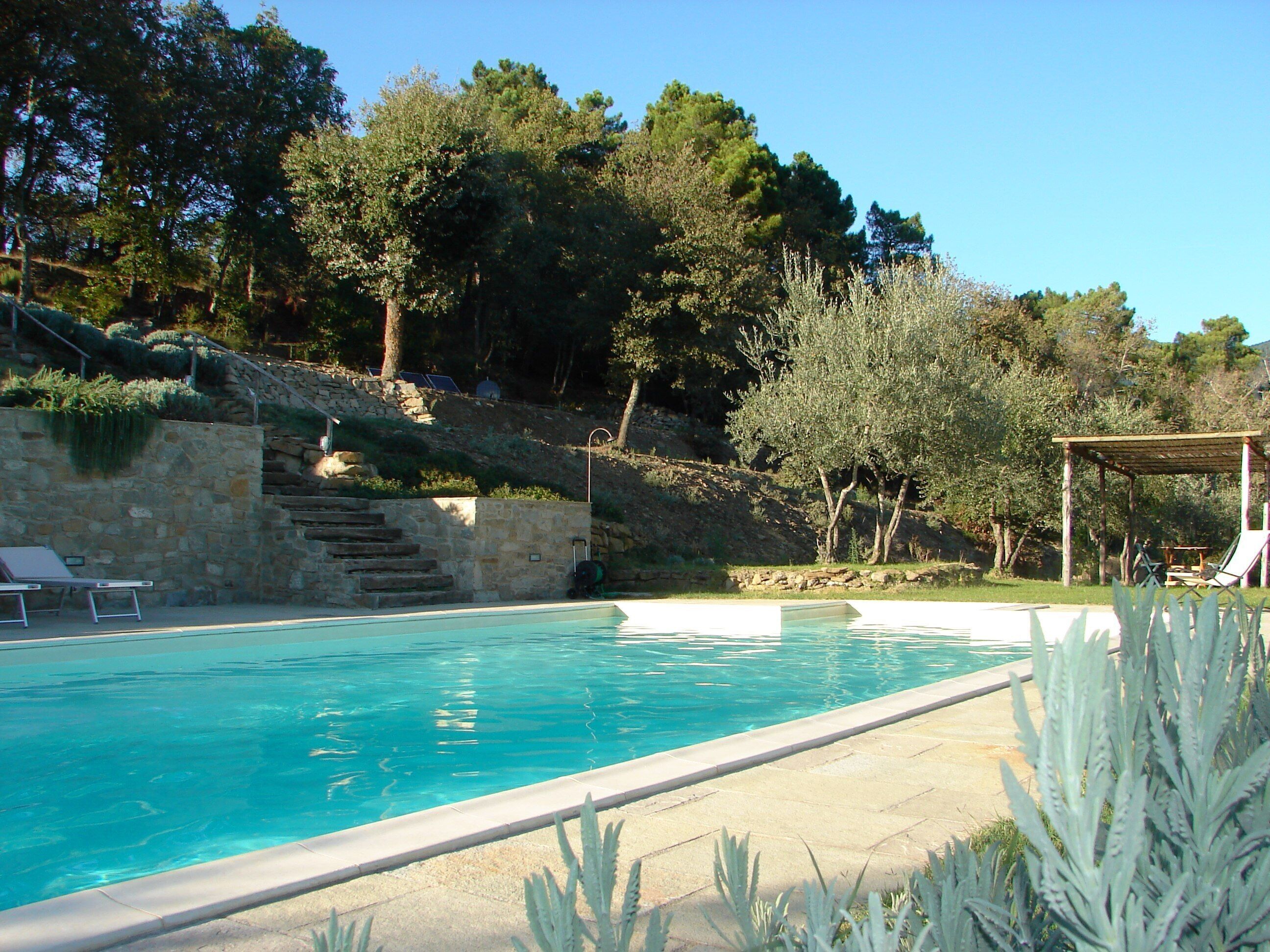 Una piscina amb una paret de pedra i unes escales que condueixen a una pérgola.