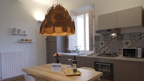 Una cocina moderna con una mesa de madera, sillas blancas, una lámpara colgante, un microondas y una estufa.