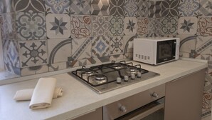 Una cocina con estufa a gas, microondas y azulejos estampados en la salpicadera.