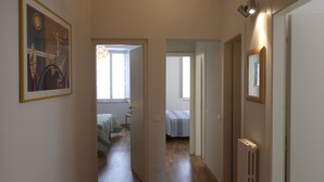 Un pasillo estrecho con una cama y un radiador a la derecha, una puerta a la izquierda y un cuadro en la pared.