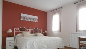 A bedroom with a bed, two bedside tables with lamps, a chair, a radiator, and a window with curtains. - Enjoy your complete rural house in Camporrotuno, Aínsa Sobrarbe (Camporrotuno)