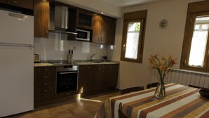 A kitchen with wooden cabinets, a microwave, and a dining area with a striped tablecloth and a vase of flowers. - Enjoy your complete rural house in Camporrotuno, Aínsa Sobrarbe (Camporrotuno)