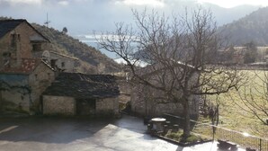 A stone building with a sloped roof, a paved area with a fence, and a view of a body of water and mountains in the background. - Enjoy your complete rural house in Camporrotuno, Aínsa Sobrarbe (Camporrotuno)