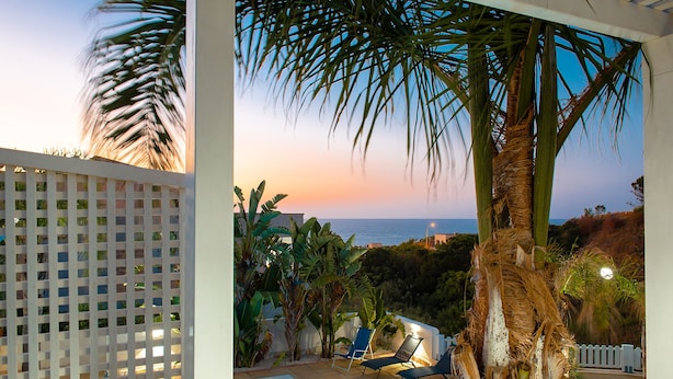 Un espace piscine avec des chaises longues, un palmier et une vue sur la mer au coucher du soleil.