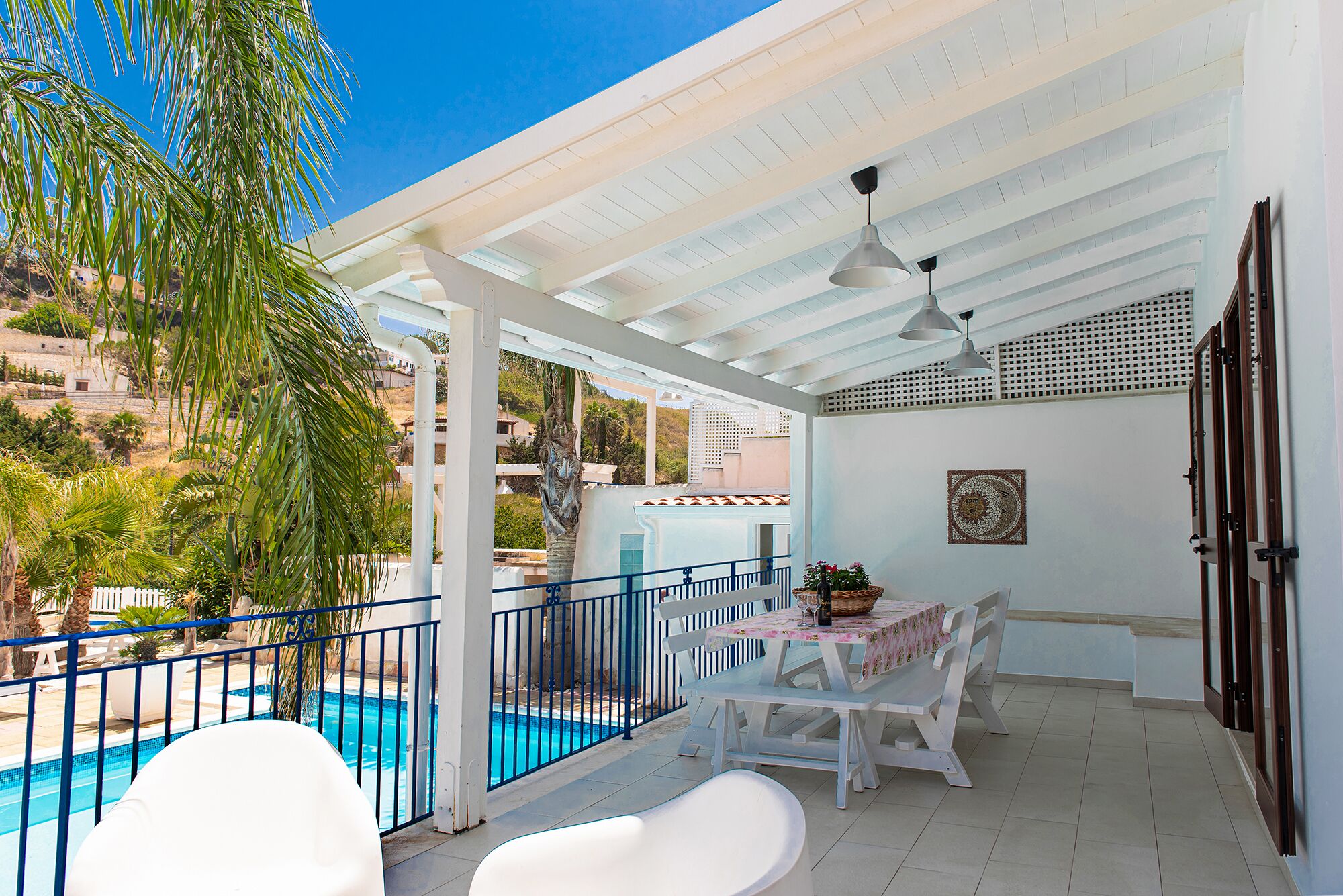 Un espacio al aire libre cubierto con piscina, mobiliario blanco y ventilador de techo.