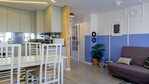 Una cocina moderna con armarios blancos, un comedor con sillas blancas, una pared azul y blanca, y un sofá púrpura.