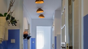 Un pasillo con paredes azules, piso de madera y una puerta a la derecha. Tres lámparas colgantes en el techo.