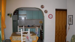 A compact kitchen with a dining area, a wooden door, and a wall clock.