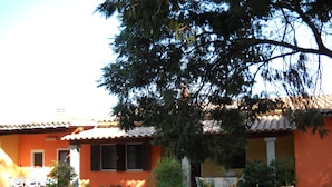 A house with a tiled roof, orange walls, and a front porch with potted plants and outdoor furniture.