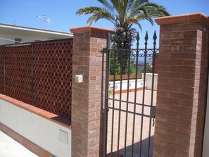 A gated entrance with a brick wall and metal gate, a palm tree, and a clear blue sky. - NEAR THE SEA AND AWAY FROM NOISES (alcamo marina)