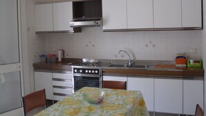 A compact kitchen with white cabinets, a stainless steel stove, a sink, and a dining table with a floral tablecloth. - NEAR THE SEA AND AWAY FROM NOISES (alcamo marina)