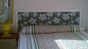 A bedroom with a wooden ceiling, a bed with floral bedding, a nightstand with a lamp, and a wall-mounted light fixture. - NEAR THE SEA AND AWAY FROM NOISES (alcamo marina)