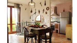 A dining area with a table set for two, surrounded by chairs. A chandelier hangs above, and various kitchen utensils are displayed on the wall. - 5-bedroom holiday apartment: nature, swimming pool, relax 30 mins from the beach (Pesaro-Urbino)