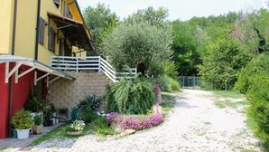 A yellow building with a white balcony, surrounded by a garden with various plants and flowers. - 5-bedroom holiday apartment: nature, swimming pool, relax 30 mins from the beach (Pesaro-Urbino)