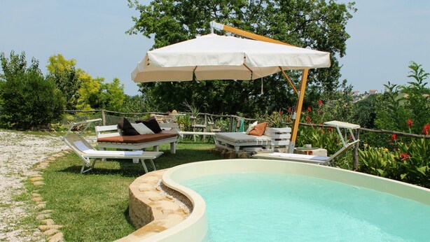 A swimming pool with lounge chairs and an umbrella. - 5-bedroom holiday apartment: nature, swimming pool, relax 30 mins from the beach (Pesaro-Urbino)