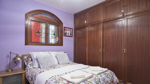 Una camera da letto con un armadio in legno, un letto con biancheria da letto a motivi floreali, un comodino con una lampada e una finestra con vetri colorati.