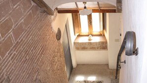 Una escalera conduce a una habitación con ventana, paredes de ladrillo y techo de vigas de madera.