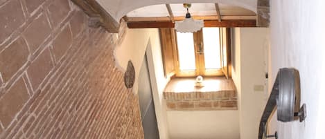 A staircase leading to a room with a window, brick walls, and a wooden beam ceiling.