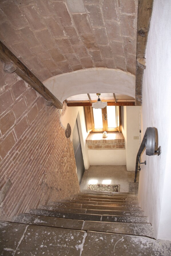 A staircase leading to a room with a window, brick walls, and a wooden beam ceiling.