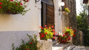 Un edificio con una escalera de piedra que conduce a una puerta de madera, macetas con flores rojas y un camino adoquinado.