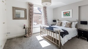 Een slaapkamer met een bed, nachtkastjes, een spiegel, een raam met gordijnen en een schilderij aan de muur.