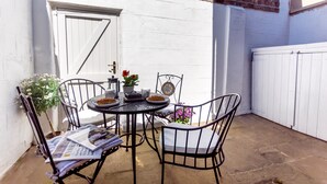Een klein terras met een ronde tafel, vier stoelen en een potplant.