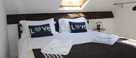 A neatly made bed with white linens, two pillows with "Love" text, a dark headboard, and a skylight above.