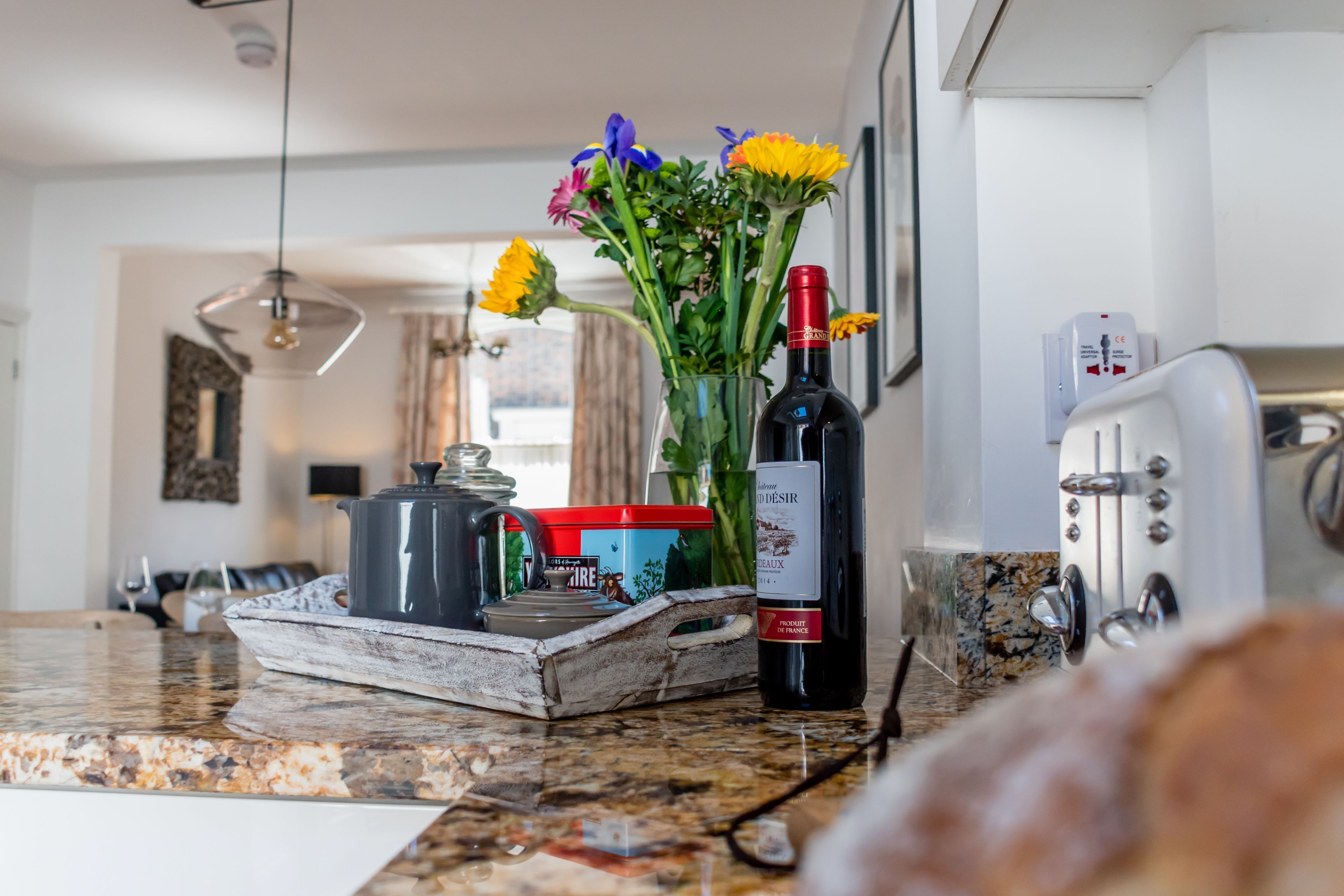 Un piano di lavoro in cucina con una bottiglia di vino, un vaso con fiori, un teiera e un vassoio.