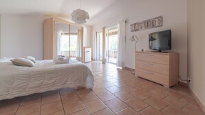 Ein Schlafzimmer mit einem Bett, einem Schminktisch, einem Fernseher und einem großen Fenster.
