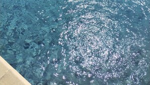 Ein klares Schwimmbecken mit Steinrand und einer Rasenfläche im Hintergrund.