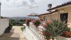 A narrow pathway leading to a balcony with a white railing, potted plants, and a view of the countryside. - Exclusive Villa with private salt pool (Case Alte)