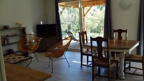 A dining area with a wooden table and chairs, a television, and a view of a garden through a large window.