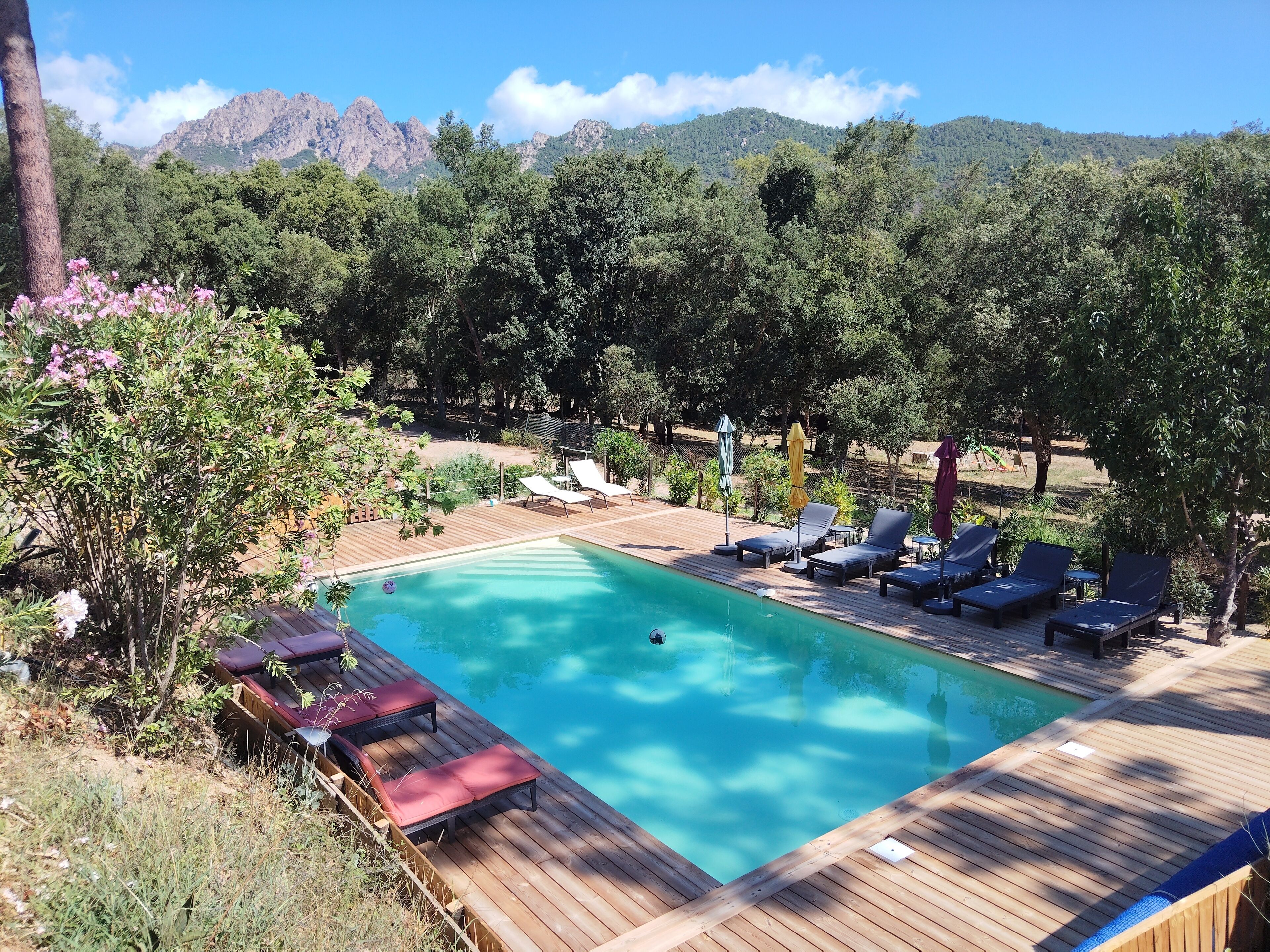 A wooden deck with a swimming pool, lounge chairs, and a view of mountains.