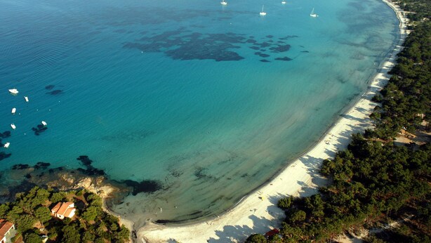 An aerial view of a coastal area with a sandy beach, clear blue waters, and several boats.