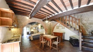 A rustic kitchen with a stone floor, wooden cabinets, and a wooden staircase.