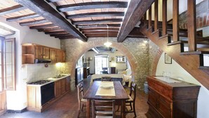 A rustic kitchen with a stone archway, wooden beams, and a dining table with chairs.