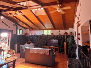 A cozy living room with a stone fireplace, wooden ceiling beams, and a television. - Wonderful typical Canarian house with outdoor pool and wifi in the mountains. (Telde)