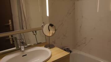 Une salle de bain avec un lavabo blanc, un miroir rond et une baignoire.