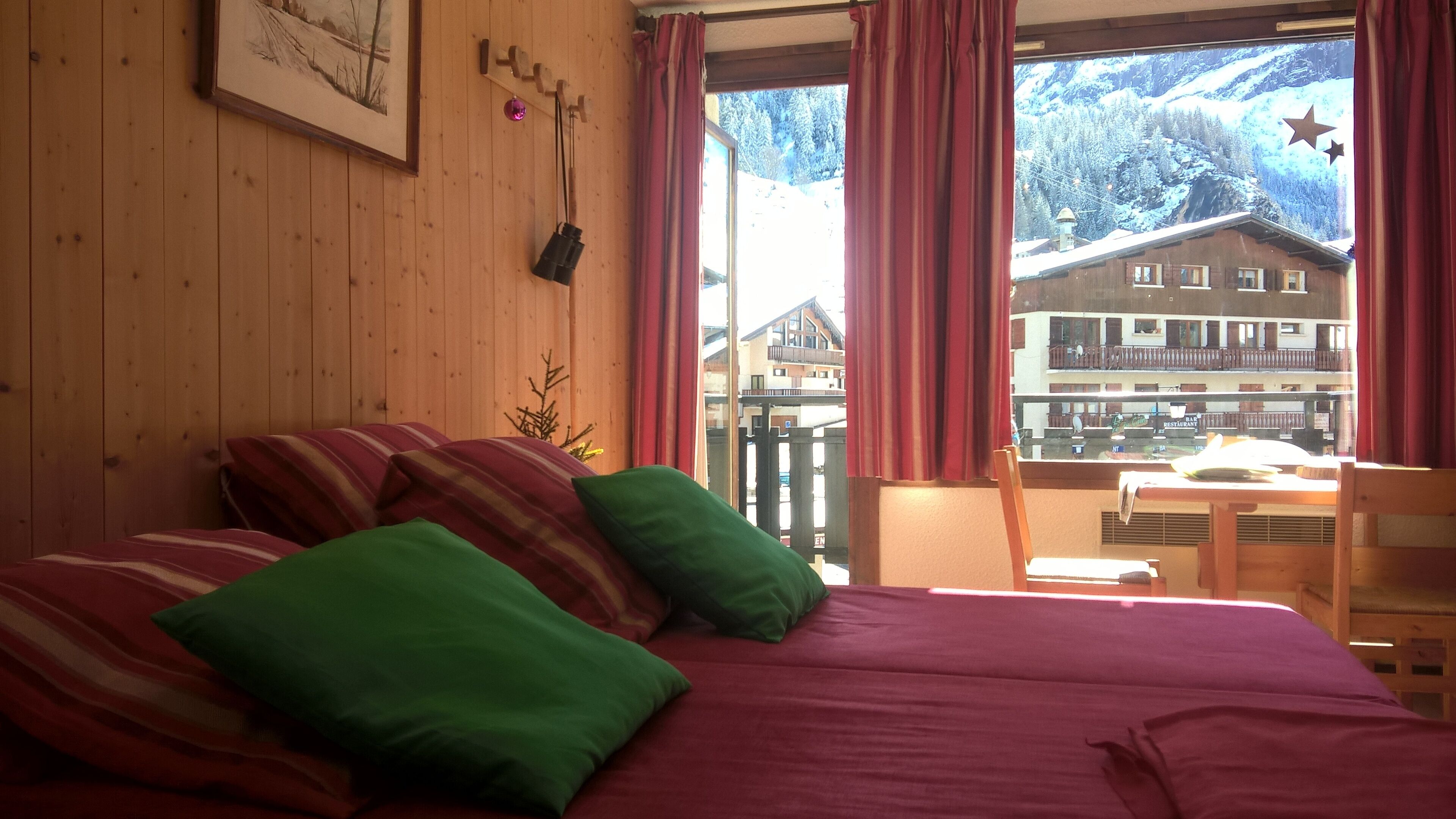 A bedroom with a bed, pillows, a window with curtains, a wooden wall, and a framed picture.