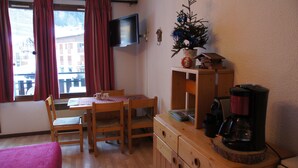 Una habitación acogedora con una mesa de madera, sillas, un pequeño árbol de Navidad, un televisor y una cafetera.