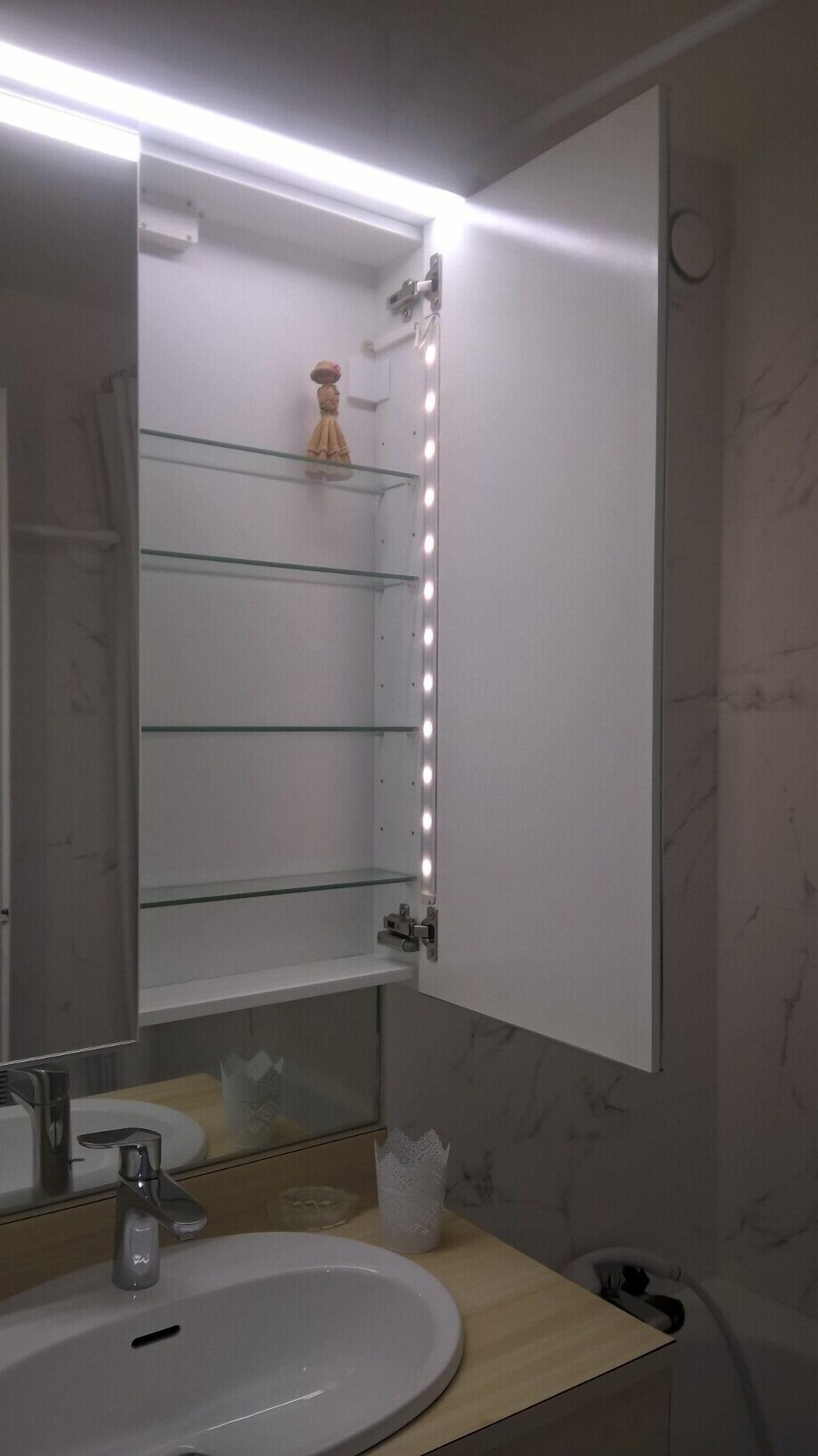 Ein Badezimmer mit Waschtisch, Spüle, Spiegel und einer Beleuchtung mit Ablagefläche.