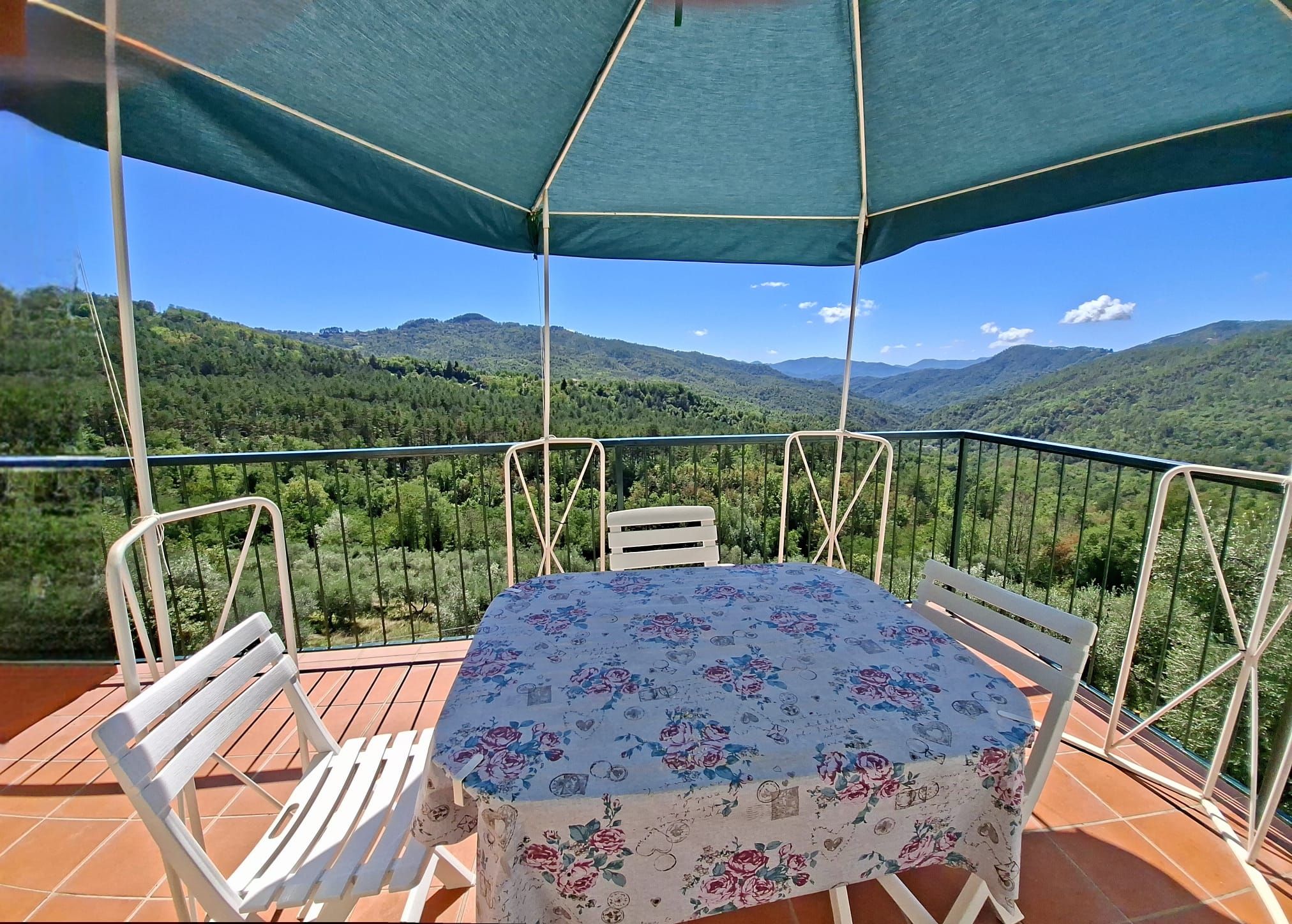 Una terraza con mesa y sillas, un parasol verde y una vista panorámica de la montaña.