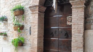 A stone building with a large wooden door, potted plants on the wall, and a cobblestone street.