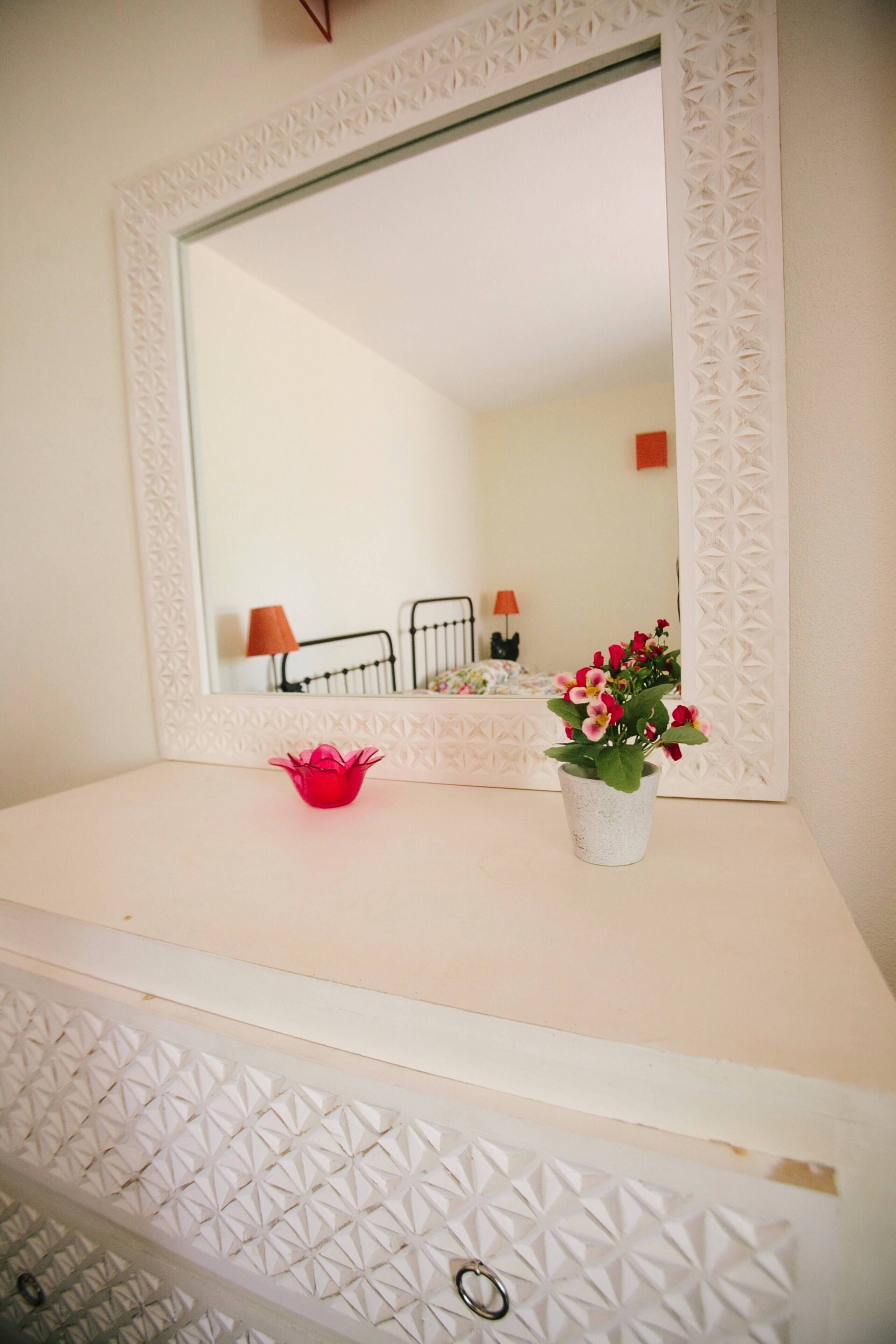 A bathroom vanity with a mirror, a small red flower vase, and a potted plant.