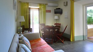 Een kamer met een bank, een eettafel met stoelen, een televisie en een raam met gordijnen.