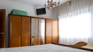A bedroom with a large bed, a wooden wardrobe, a television mounted on the wall, and a chandelier. - The apartment is an 8-minute walk from Venice/Mestre ferrrov. station. (Venezia)