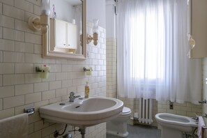 Een bad/douchecombinatie, een bidet, handdoeken, zeep